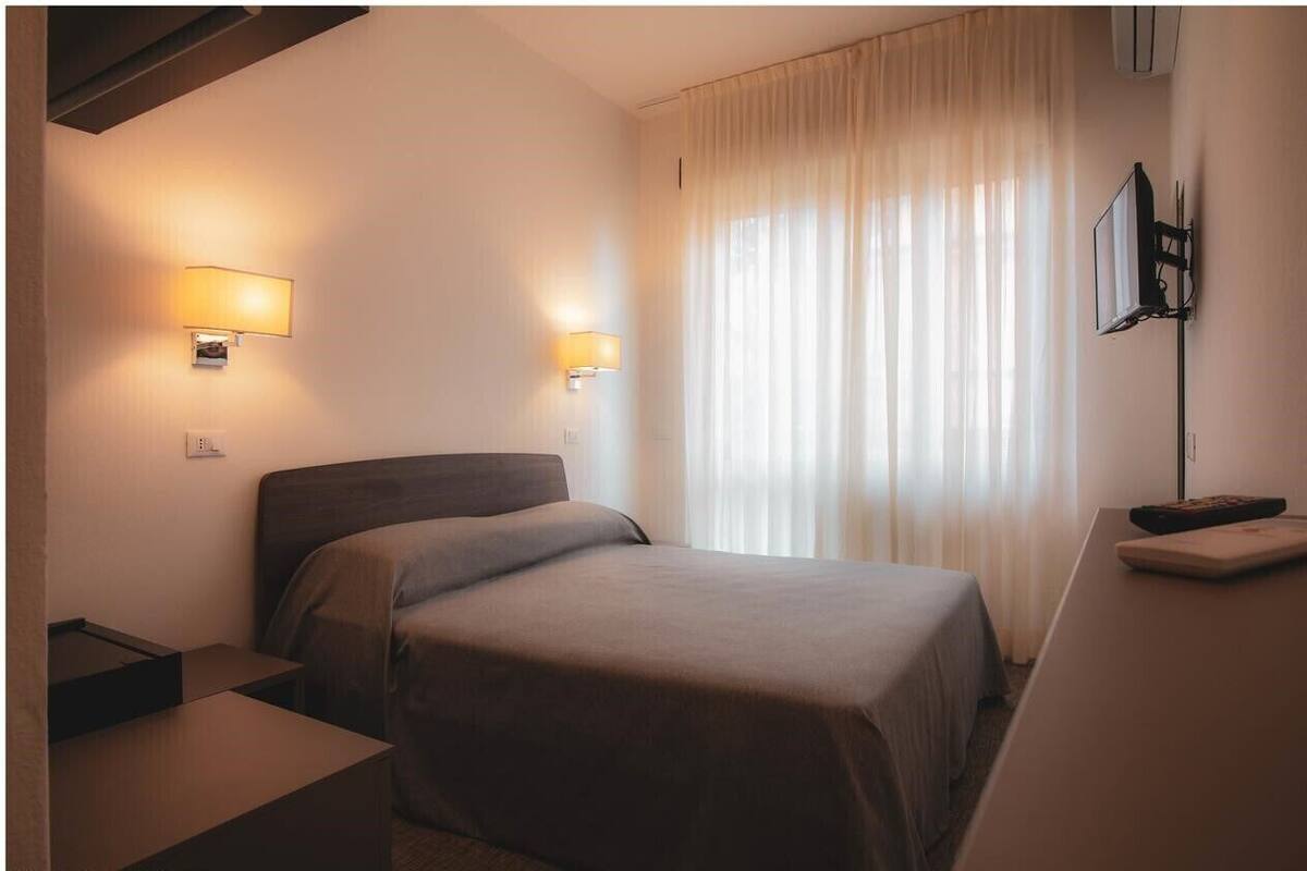 A hotel room with a bed, bedside tables, a desk, and a TV mounted on the wall.