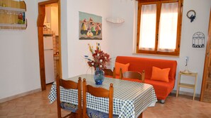 A dining area with a checkered tablecloth, wooden chairs, and a red sofa.
