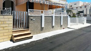 A two-story residential building with a balcony, a stone wall, and a metal gate.