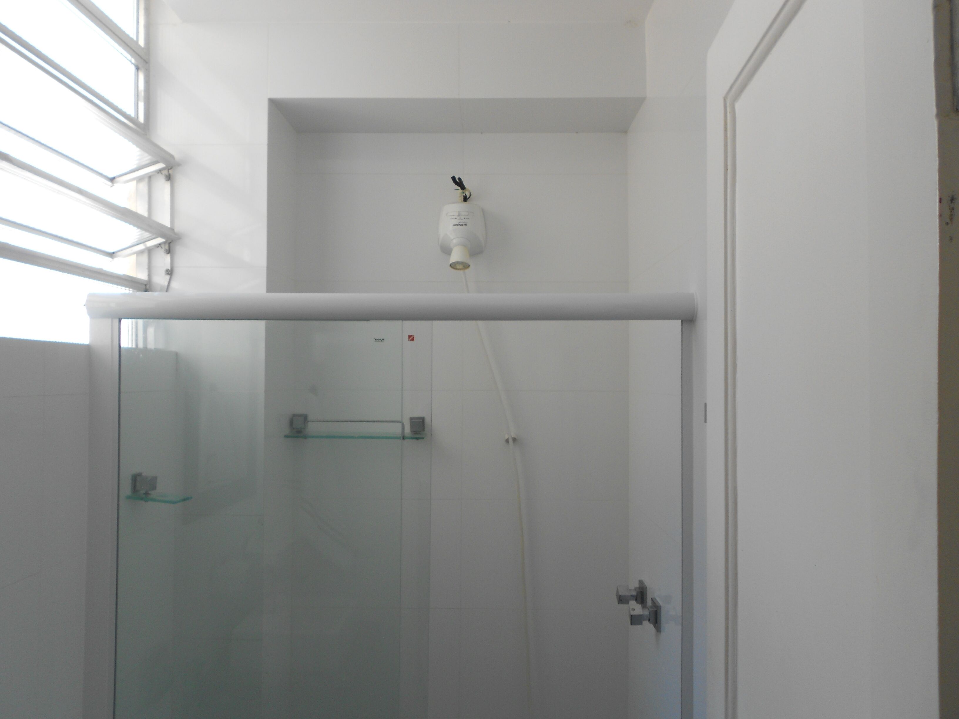 A glass-enclosed shower with a glass shelf and a white ceiling light fixture.