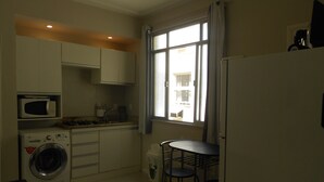 A compact kitchen with a washing machine, microwave, and a small dining area with two stools. - Gohouse - Nabuco 604 (Rio de Janeiro)