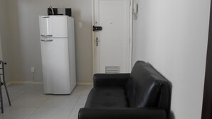 A compact living space with a white refrigerator, a black leather sofa, and a white door. - Gohouse - Nabuco 604 (Rio de Janeiro)
