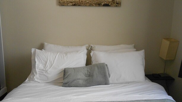A neatly made bed with white and gray linens, a single gray pillow, and a framed picture of a cityscape with a tower on the wall above it. - Gohouse - Nabuco 604 (Rio de Janeiro)