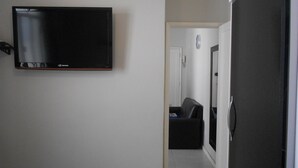 A hallway with a mounted television, a door, and a small seating area. - Gohouse - Nabuco 604 (Rio de Janeiro)