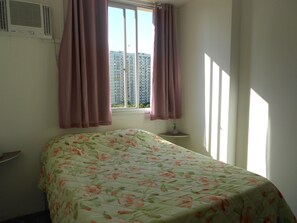A bedroom with a floral bedspread, a window with pink curtains, and a radiator on the wall.
