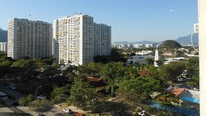 Un edificio residencial alto con varios balcones, rodeado de vegetación y otros edificios.