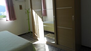 Una habitación con cama, armario, ventana con cortinas y una planta verde.