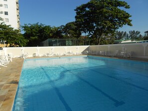 A swimming pool with clear blue water, surrounded by white lounge chairs and a white wall.