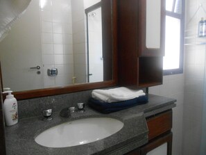 Un baño con lavamanos blanco, un espejo, una toalla y artículos de aseo.