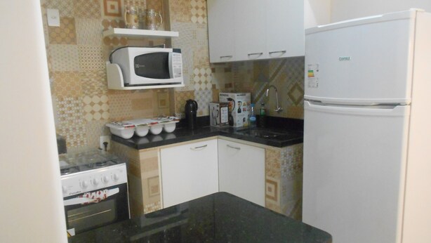 A compact kitchen with a stove, microwave, sink, and refrigerator. - Gohouse - Riachuelo 306 B (Rio de Janeiro)