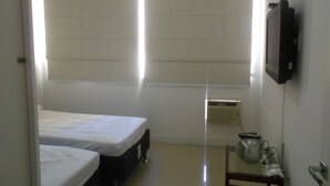 A small, sparsely furnished room with two single beds, a television on the wall, and a radiator. - Gohouse - Riachuelo 306 B (Rio de Janeiro)