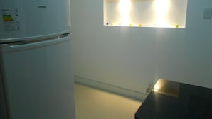 A kitchen with a white refrigerator, a black countertop, and a wall-mounted light fixture. - Gohouse - Riachuelo 306 B (Rio de Janeiro)