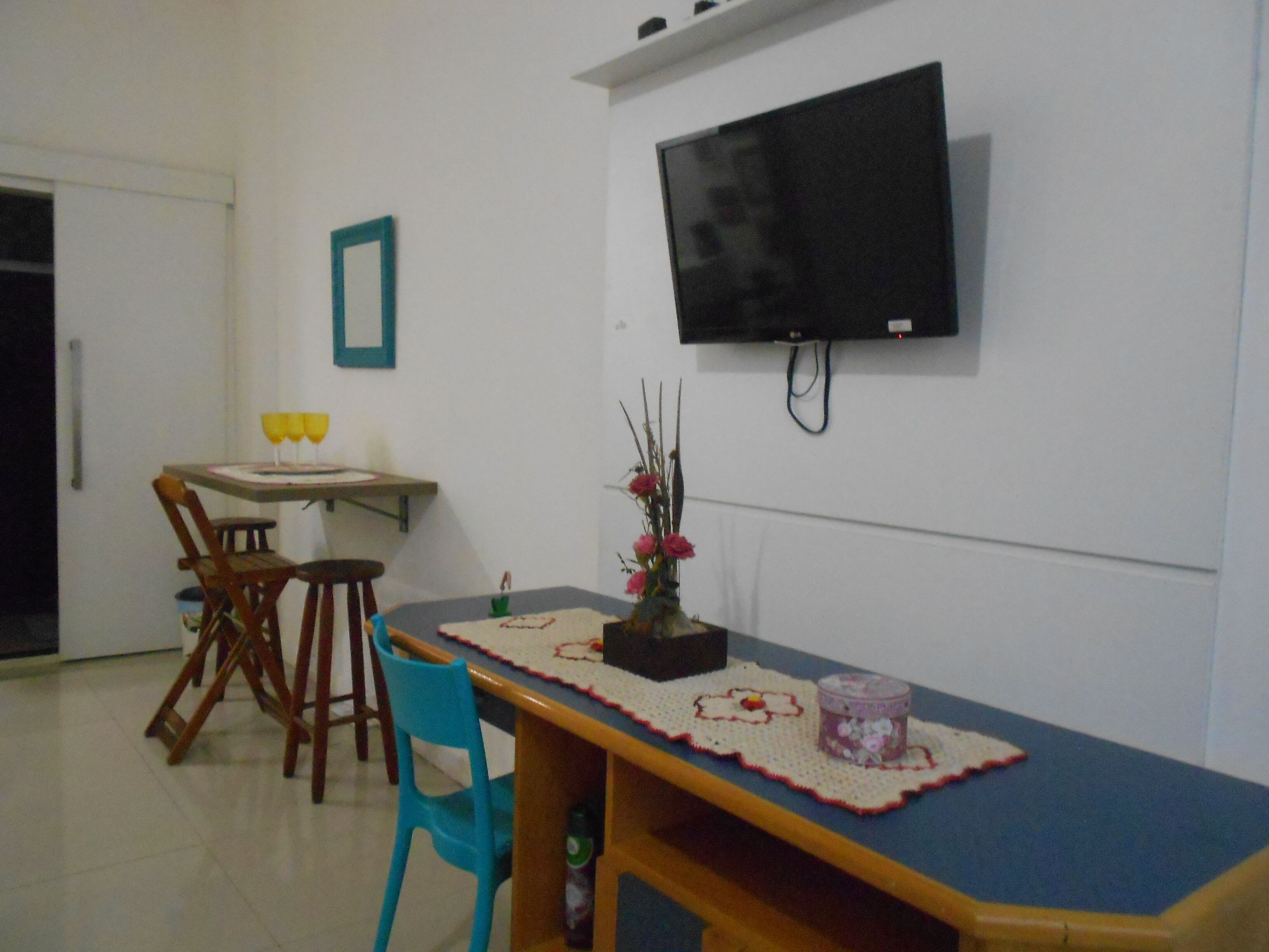 A dining area with a table, chairs, a vase with flowers, and a television mounted on the wall.