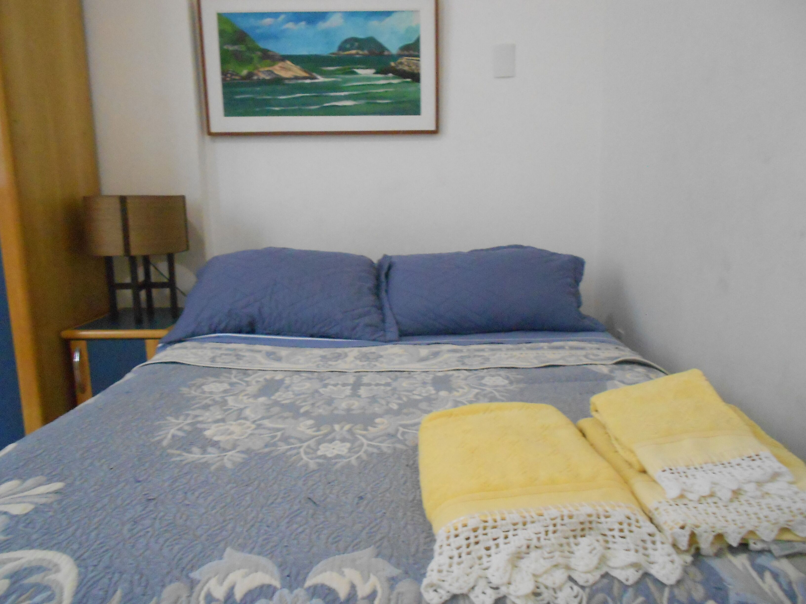 Una camera da letto con un letto, cuscini, una lampada e un quadro appeso al muro.