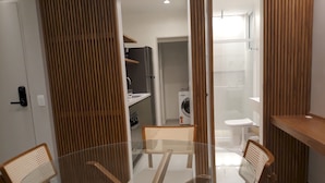 A modern kitchen with a glass dining table, wooden chairs, and a built-in washing machine. - Gohouse - Ataulfo 201 (Rio de Janeiro)