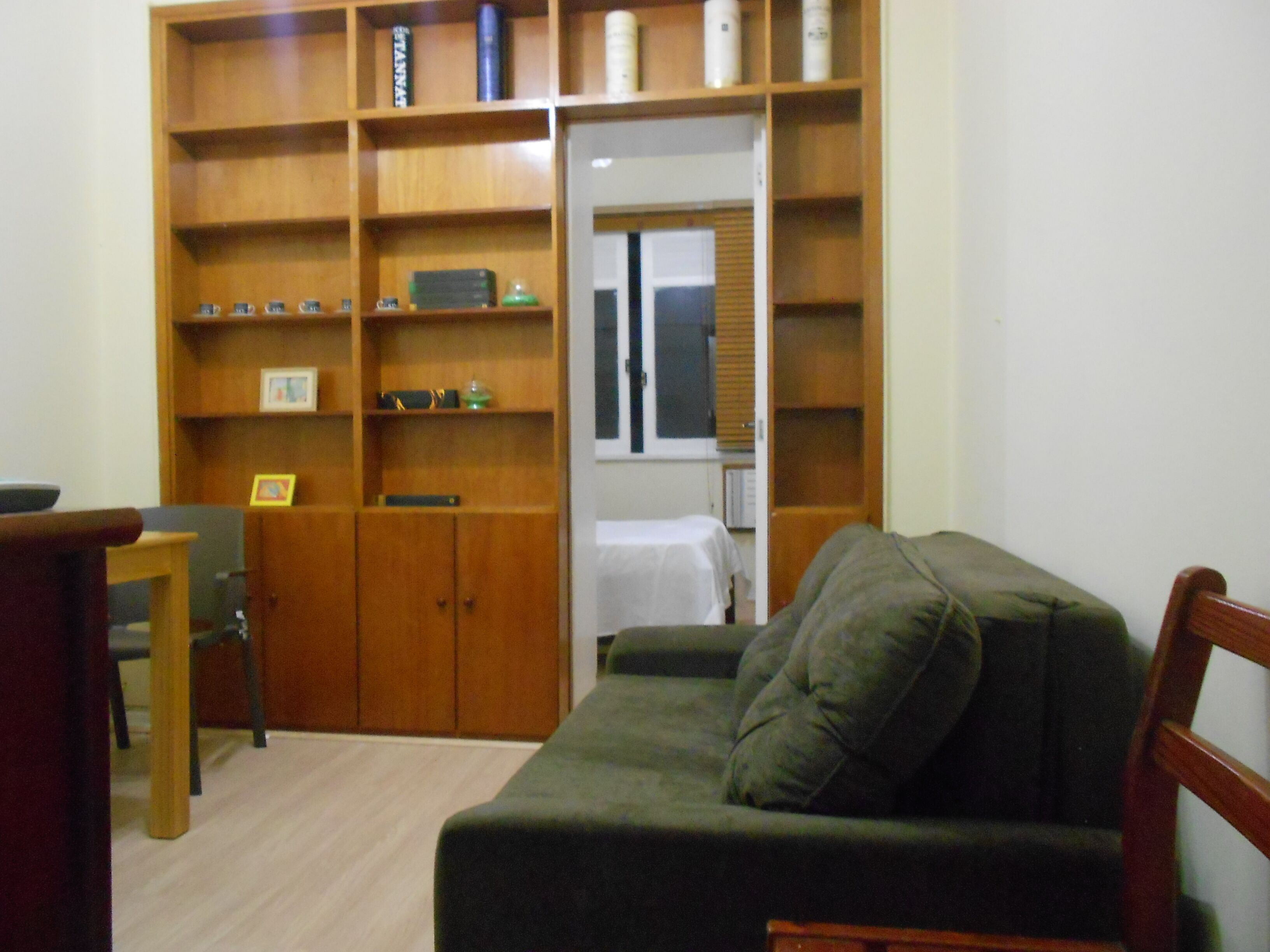 Une pièce avec une bibliothèque en bois, un canapé vert, une chaise en bois et une petite table.