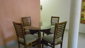 A dining area with a round glass table surrounded by four wooden chairs with cushioned seats. - Gohouse - Visconde 402 B (Rio de Janeiro)