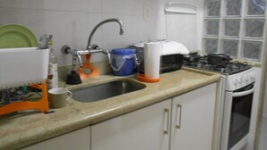 A kitchen with white cabinets, a sink, a stove, and various kitchen items. - Gohouse - Visconde 402 B (Rio de Janeiro)