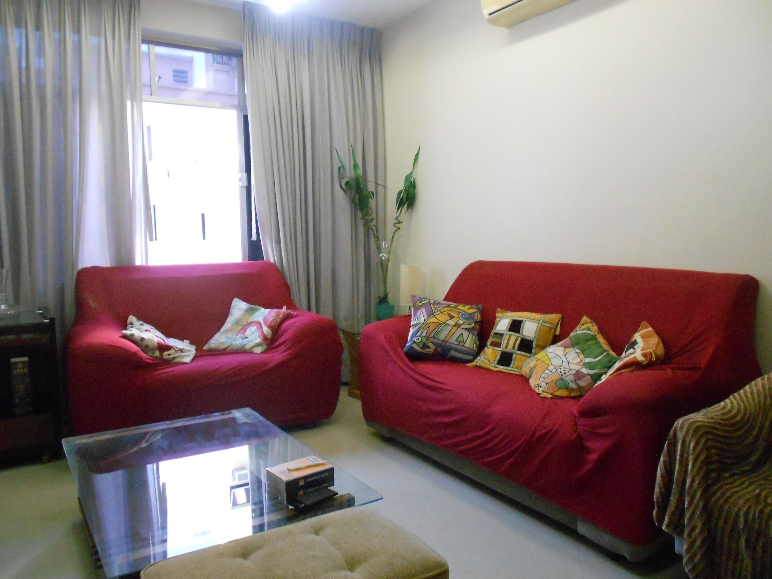 A living room with a red sofa, a glass coffee table, and a potted plant.