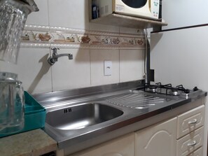 Kitchen area with a stainless steel sink, gas stove, and microwave, set against a decorative tiled backsplash.