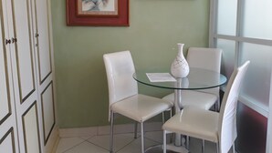 A room with a glass table, white chairs, a white vase, and two framed artworks on the wall. - Gohouse - Siqueira 1417 (Rio de Janeiro)