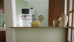 A kitchen with a microwave, a yellow pot, and two white stools. - Gohouse - Ferreira 76 (Rio de Janeiro)