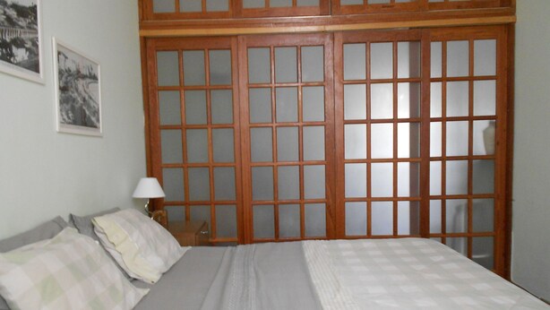 A bedroom with a large bed, a nightstand with a lamp, and a wooden shoji screen door. - Gohouse - Ferreira 76 (Rio de Janeiro)