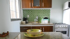 A kitchen with wooden cabinets, a green tiled backsplash, a stove, and a sink. - Gohouse - Ferreira 76 (Rio de Janeiro)