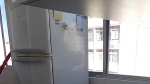 Une cuisine avec un réfrigérateur blanc, une fenêtre et des murs carrelés.