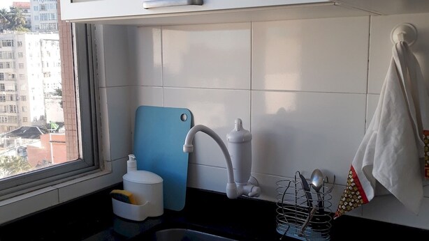Une cuisine avec un plan de travail noir, des meubles blancs, une fenêtre et une vue sur les bâtiments à l’extérieur.