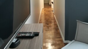 Ein schmaler Flur mit Holzboden, einem Bett auf der rechten Seite und einem Fernseher auf der linken Seite.
