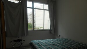 Une pièce avec un lit, une chaise, une fenêtre et un radiateur.