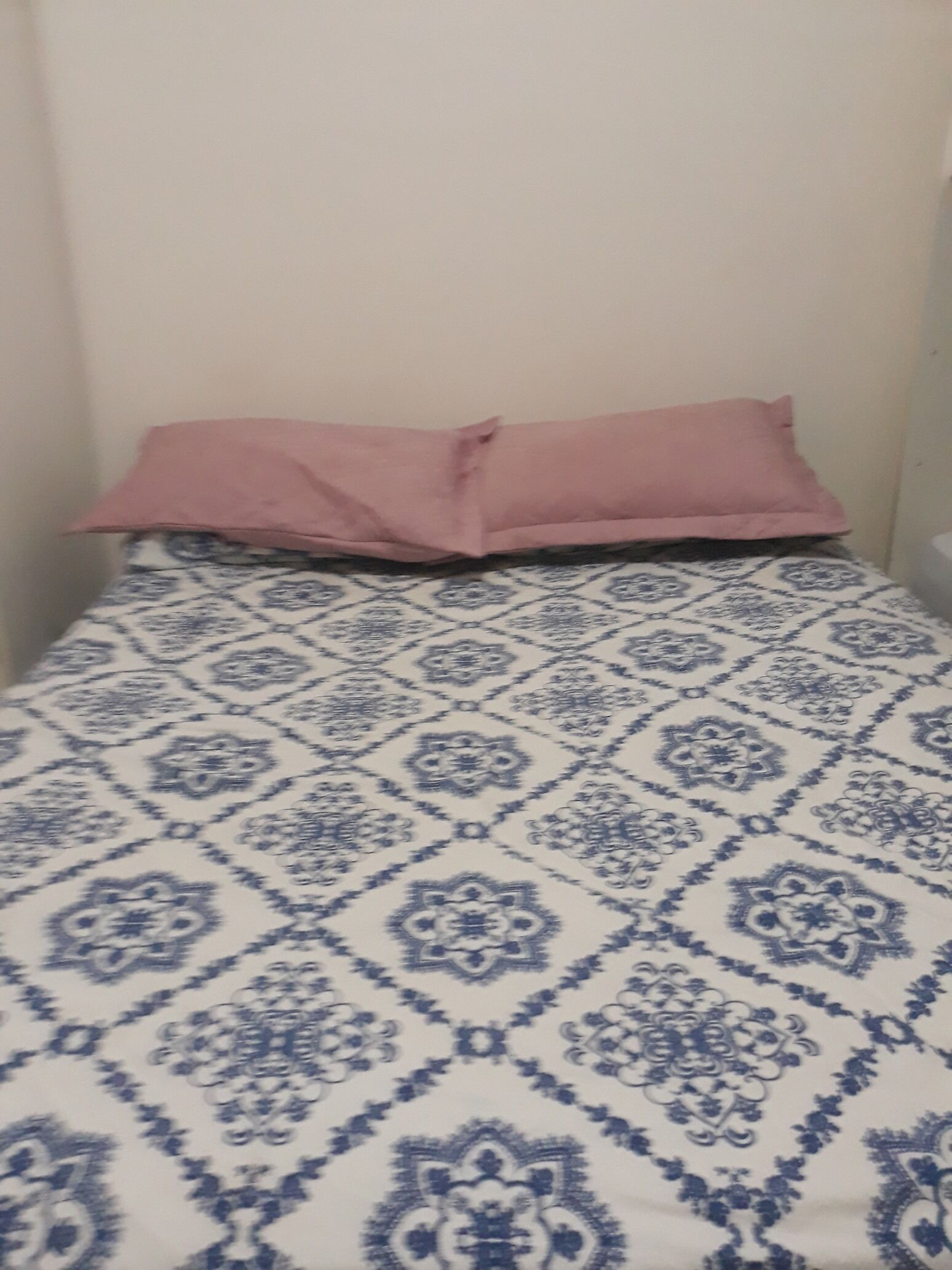 Ein Bett mit einem gemusterten Bettbezug und einem rosafarbenen Kopfkissen.