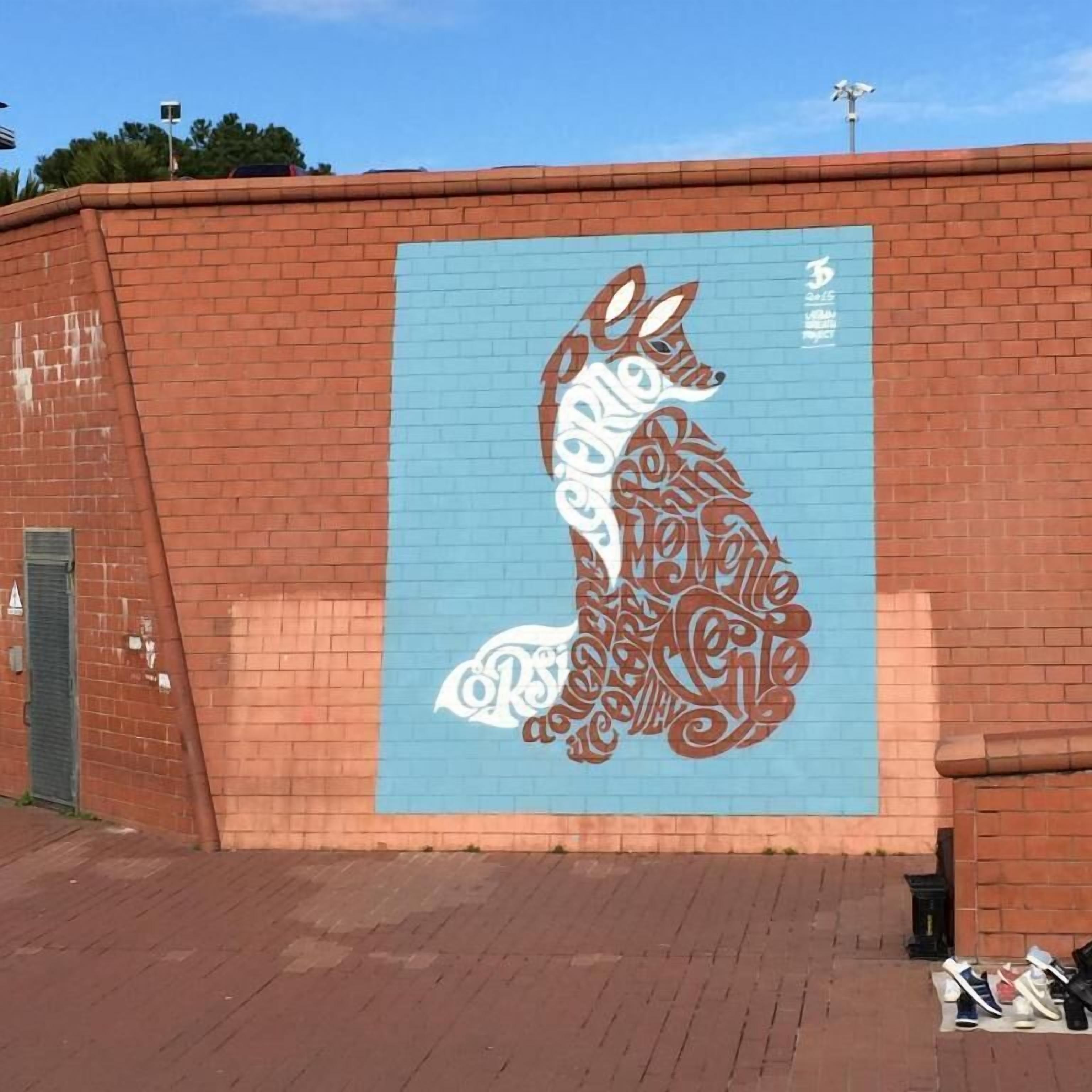 Une fresque représentant un renard stylisé, peinte sur un mur de briques.