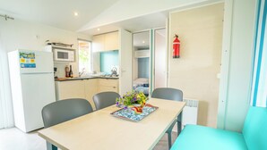 A compact kitchen with a microwave, sink, and a small dining area with a table and chairs. A fire extinguisher is mounted on the wall. - Happy Camp in Amadria Park Camping Trogir (Seget)