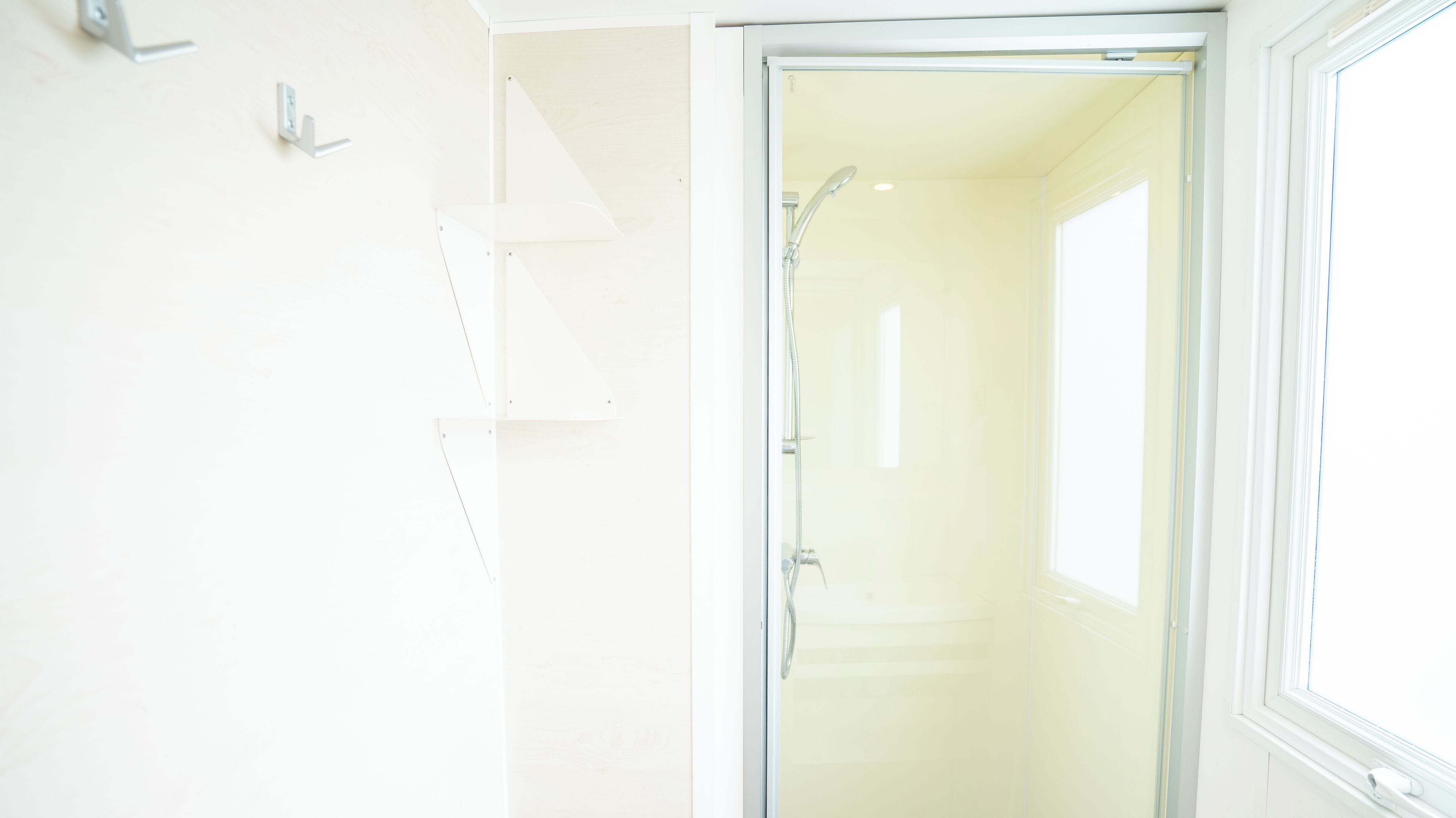 Een badkamer met een douchecabine van glas, een witte muur en een raam.