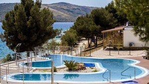 A swimming pool with a view of the sea and hills, surrounded by trees and a covered area with a roof. - Happy Camp in Amadria Park Camping Trogir (Seget)