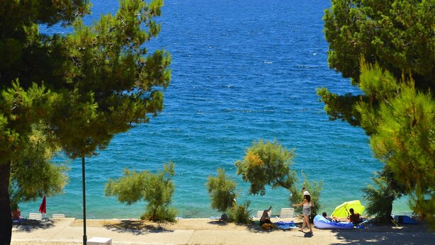A coastal view with clear blue sea, a sandy beach, and pine trees. - Happy Camp in Amadria Park Camping Trogir (Seget)