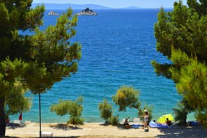 A coastal view with clear blue sea, a sandy beach, and pine trees. - Happy Camp in Amadria Park Camping Trogir (Seget)