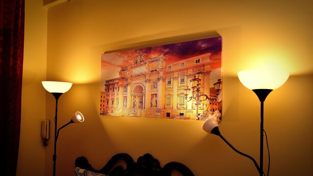 A room with a bed, two wall-mounted lamps, and a large painting of a building. - Tiberius Suite Roma (Rome)
