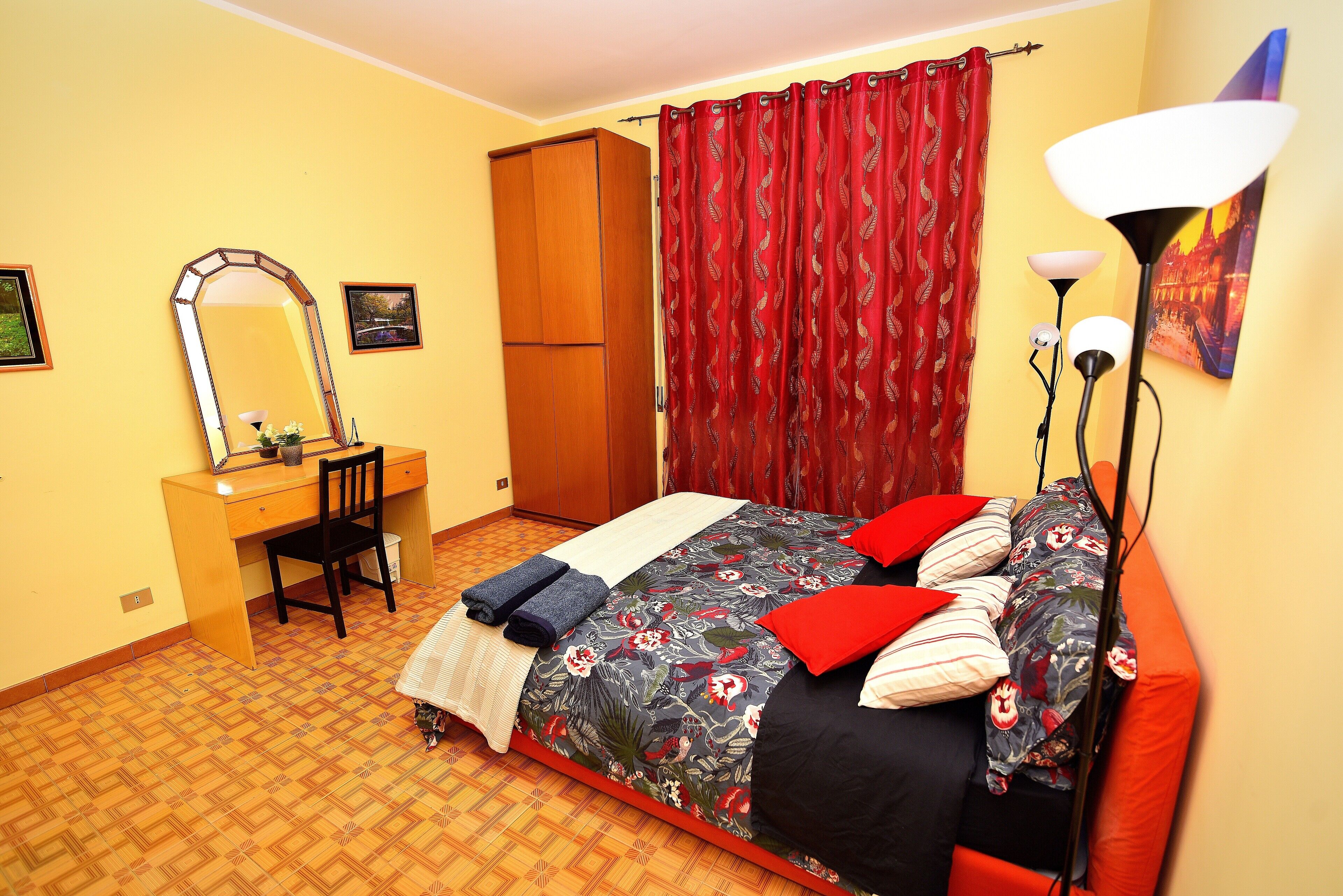Quarto com cama, escrivaninha, cadeira, guarda-roupa e um espelho grande.