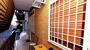 A narrow corridor with a wooden table and two chairs, a window with blinds, and a door with a metal gate. - Tiberius Suite Roma (Rome)