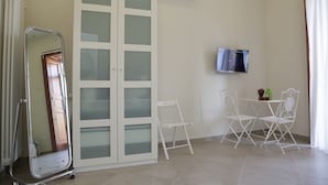 A room with a white wardrobe, a small table with chairs, a television, and an air conditioning unit. - Sun&TheCity (Naples)