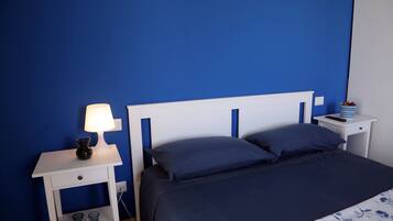 Un dormitorio con una cama, una mesita de noche con lámpara y una pequeña mesa con mando a distancia.