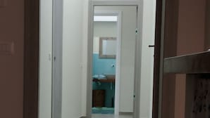 A hallway leading to a bathroom with a sink and mirror. - Sun&TheCity (Naples)