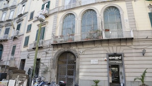 A building with a storefront named "Gimaro" featuring a signboard, a large arched entrance, and a balcony with potted plants. - Sun&TheCity (Naples)