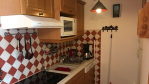 A kitchen with wooden cabinets, a stove, a coffee maker, and a mop. - Cozy apartment in Montgenèvre - Close to slopes - South-facing terrace (Montgenèvre)