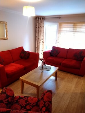 A living room with two red sofas, a wooden coffee table, and a patterned armchair. - Victoria Cloisters Apartments (York)