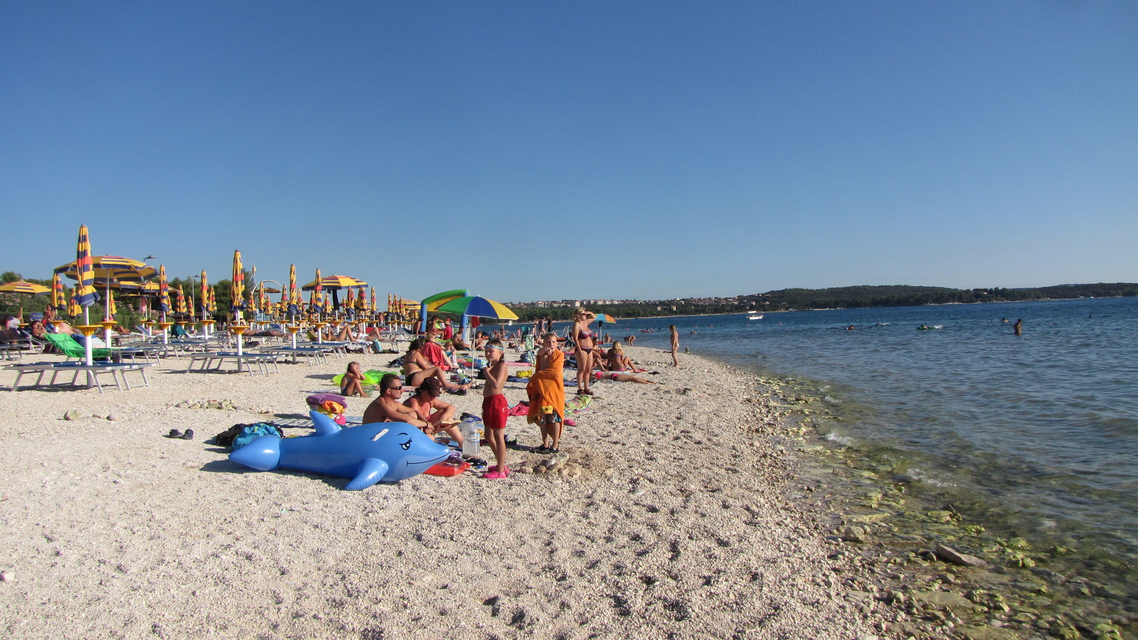 A beach with sun loungers and umbrellas, a clear sky, and a calm sea.