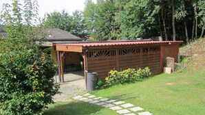A covered outdoor area with a wooden structure, a stone pathway, and a garden with sunflowers. - Holiday house without everyday noise (Altomünster)